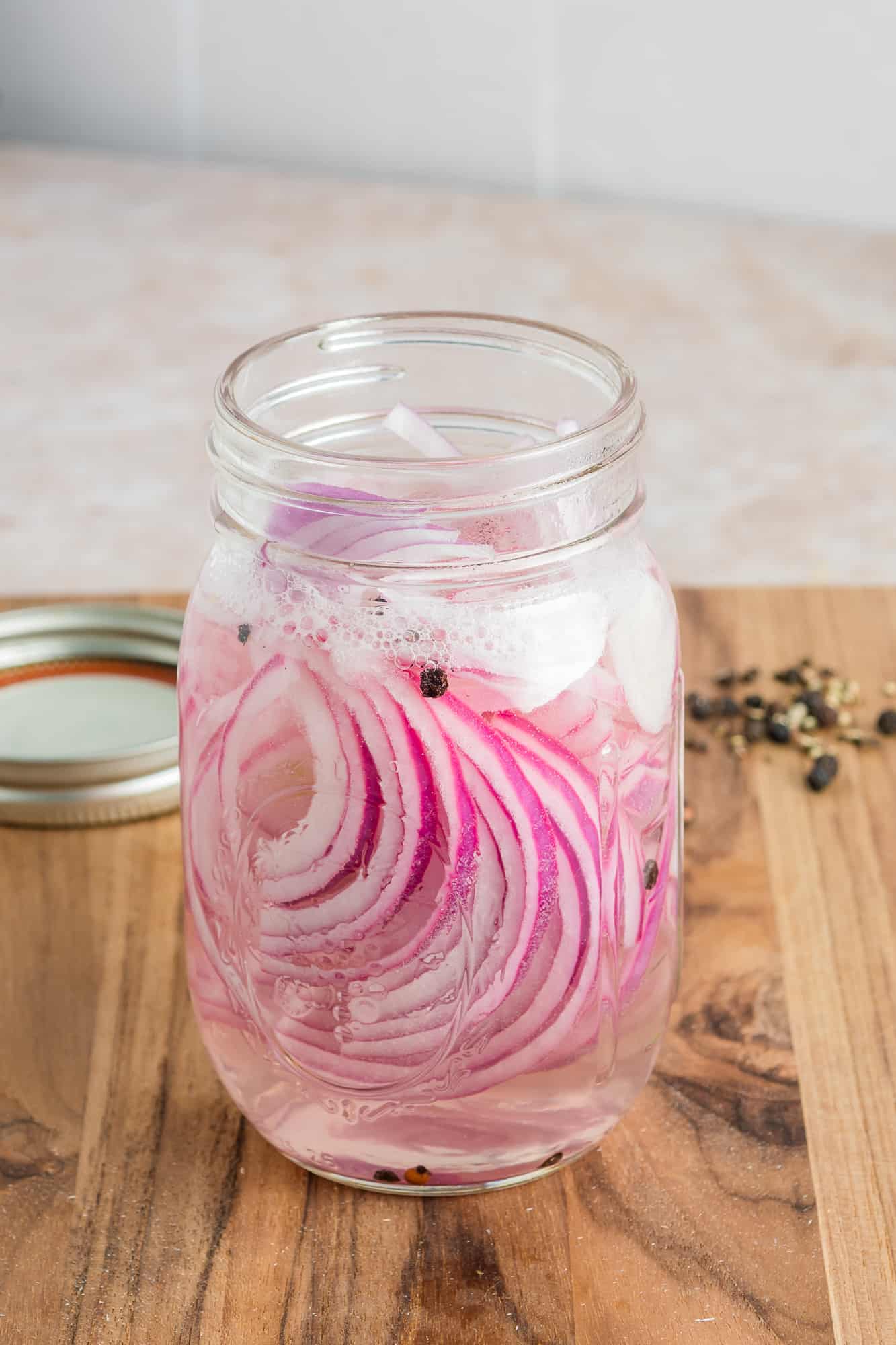 Red onions and ingredients placed into a mason jar.