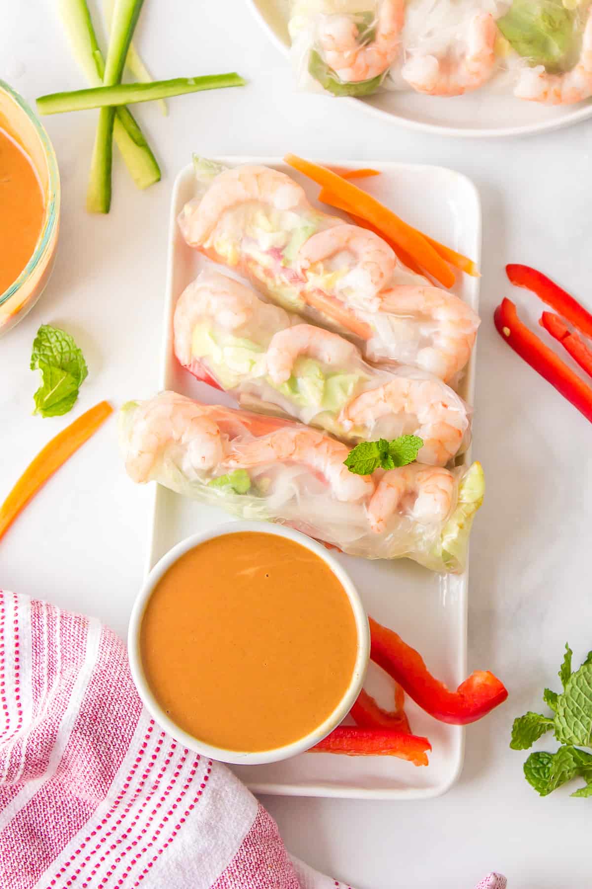 A serving platter of three vietnamese shrimp rolls with peanut sauce on the side.