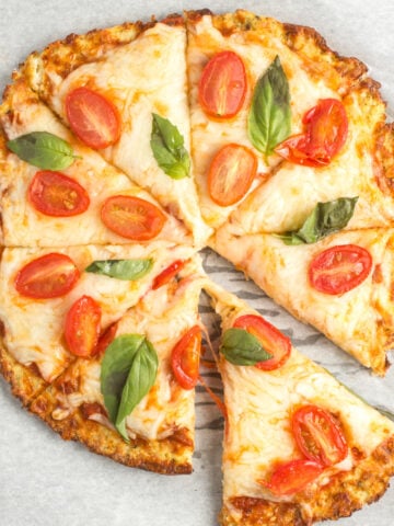 Cooked cauliflower pizza with a slice taken out.