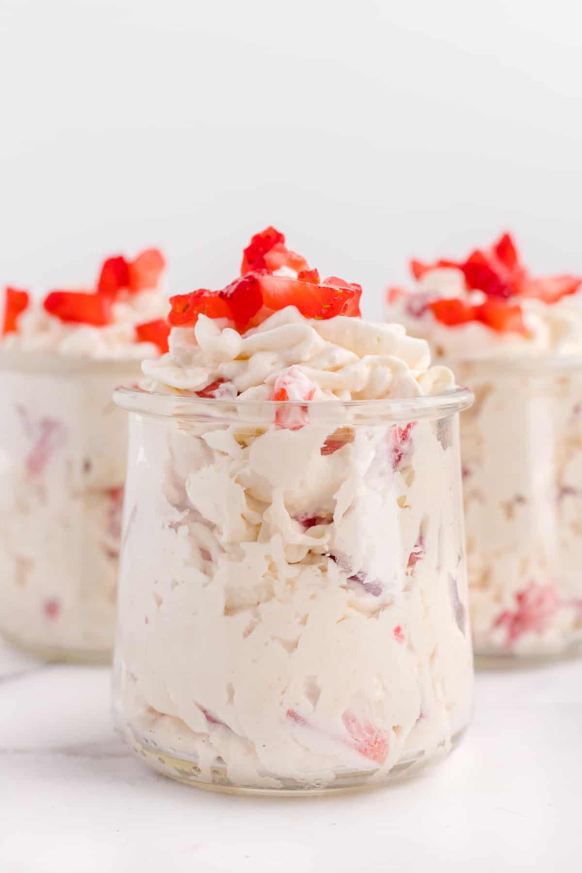 Three jars of keto cheesecake fluff topped with strawberries.