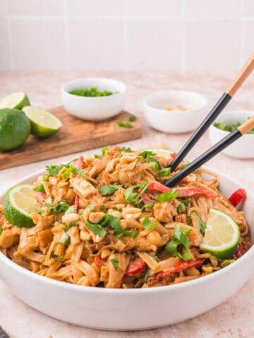 Garnished and served bowl of thai peanut noodles with chop sticks.