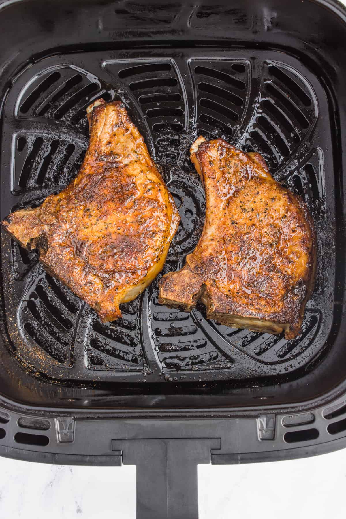 Two cooked pork chops in the air fryer basket.