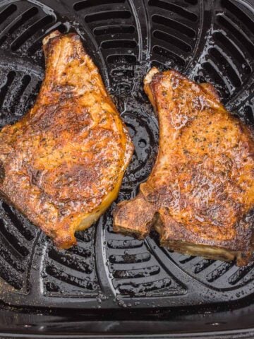 Two cooked pork chops in the air fryer basket.