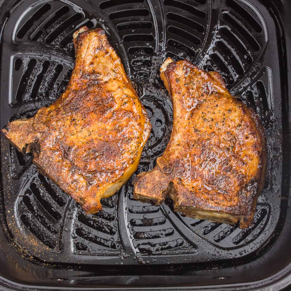 Two cooked pork chops in the air fryer basket.