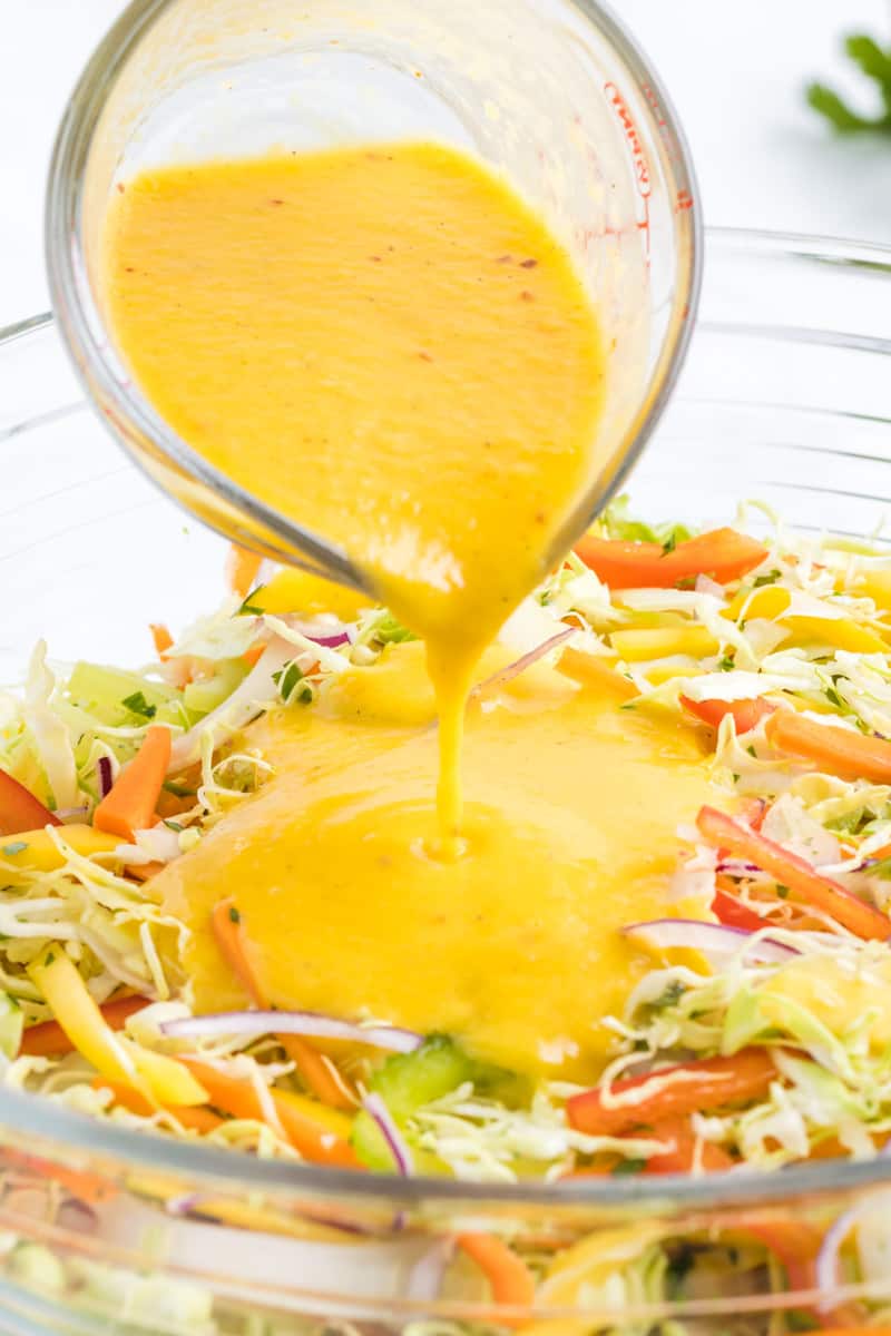 mango dressing being poured on top of the slaw.