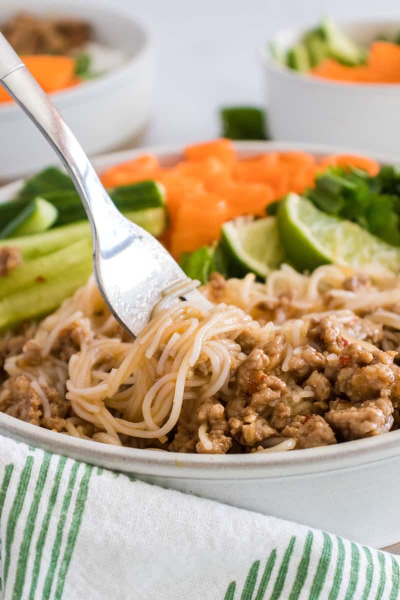 A fork in a pork bowl twirling up the noodles.