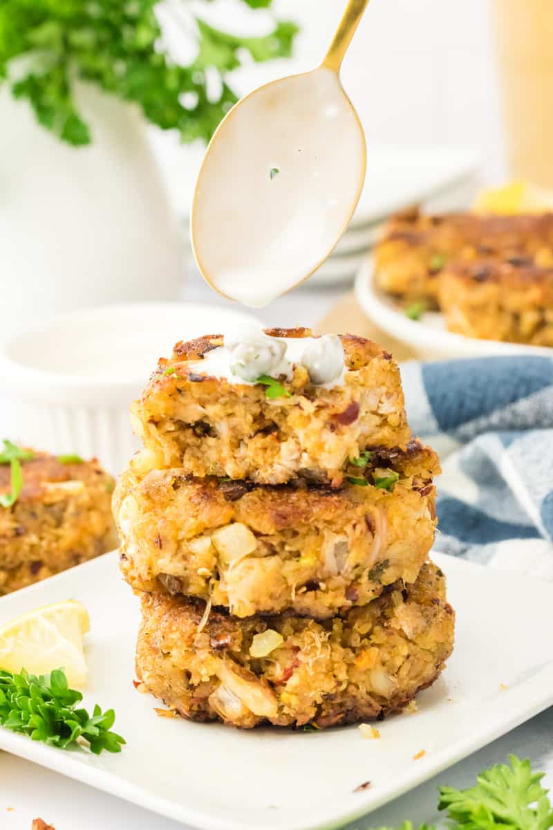 A stack of crab cakes being drizzled in sauce.