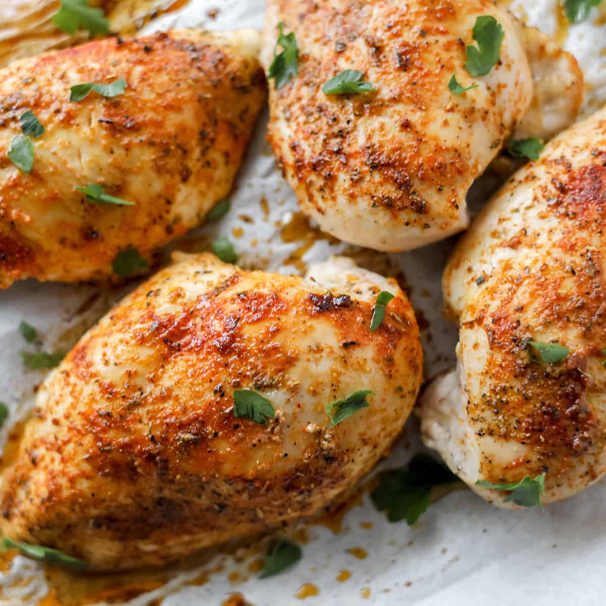 close up of baked whole boneless skinless chicken breasts on a white cutting board