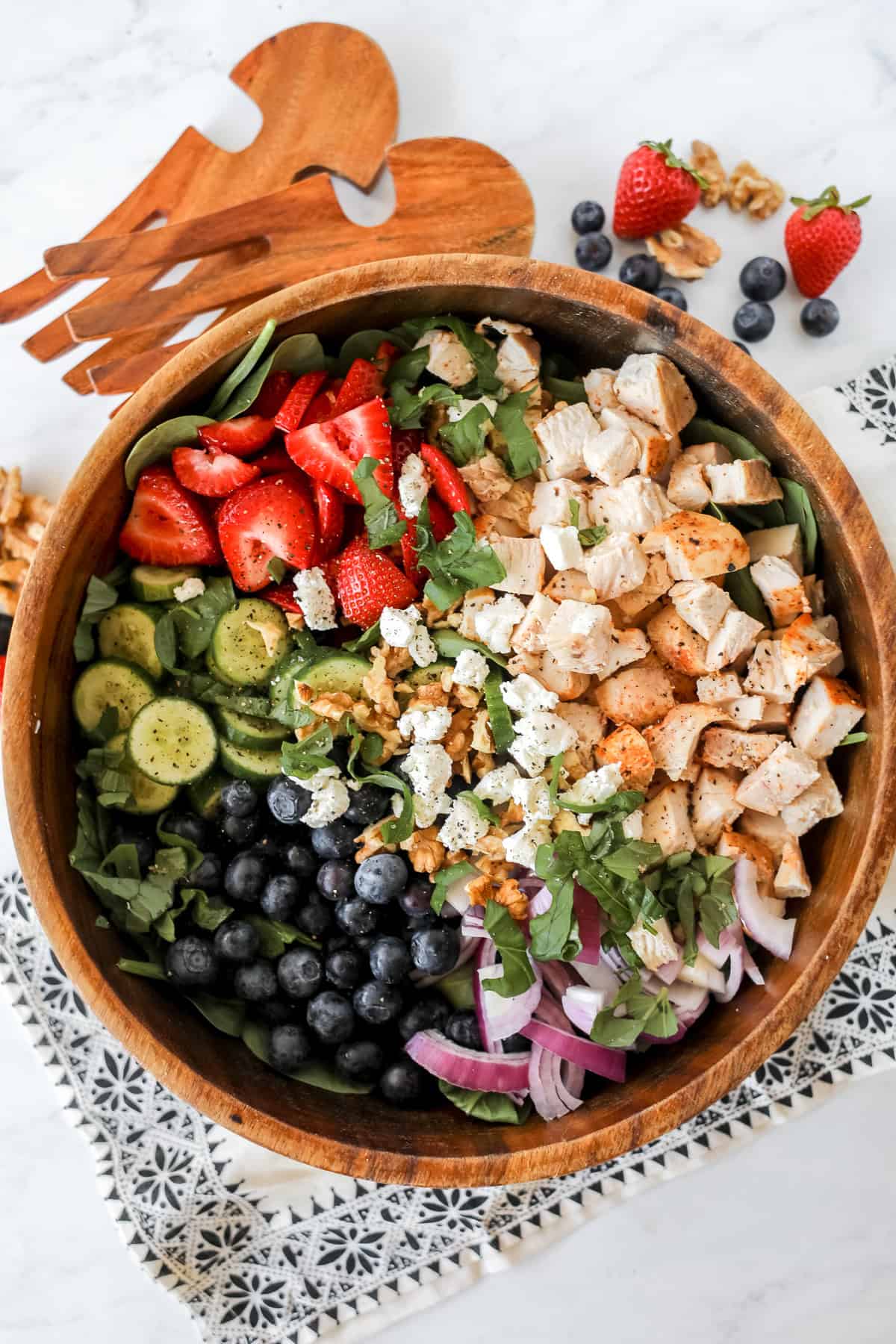 chicken salad with strawberries blueberries and cucumbers on a bed of spinach ready to serve with salad tongs