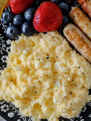 scrambled eggs with cottage cheese on a black plate after cooking in a skillet