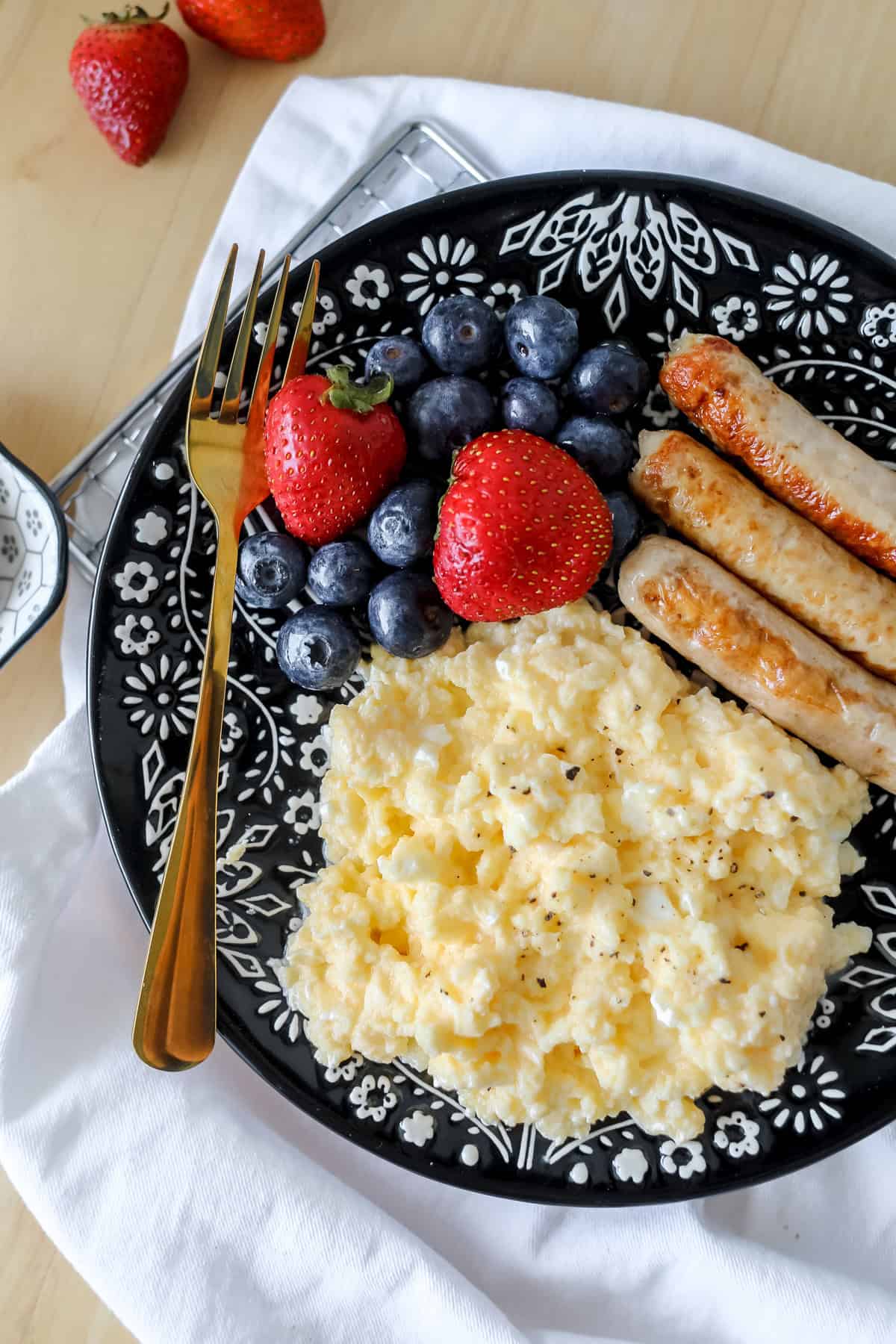 cottage cheese eggs on a black plate with fruit and chicken sausage