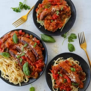 chicken sausage and peppers on two plates and the rest on a black platter
