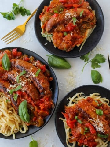 chicken sausage and peppers on two plates and the rest on a black platter