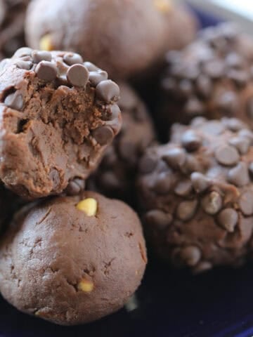 close up of chocolate peanut butter protein balls on a blue plate with a bite taking out of one.