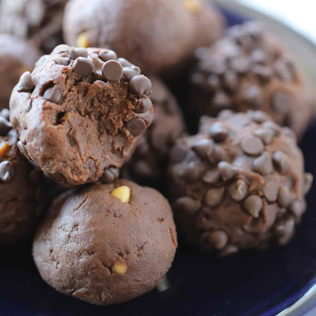 close up of chocolate peanut butter protein balls on a blue plate with a bite taking out of one.
