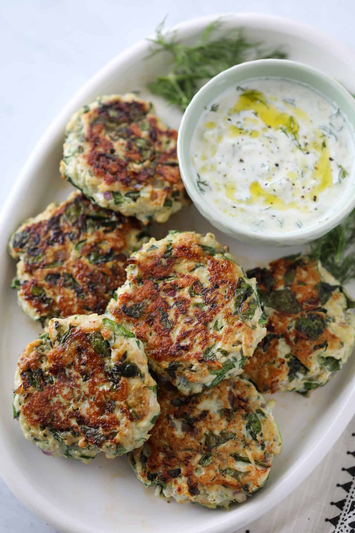 greek turkey patties on a white platter with tzatziki sauce