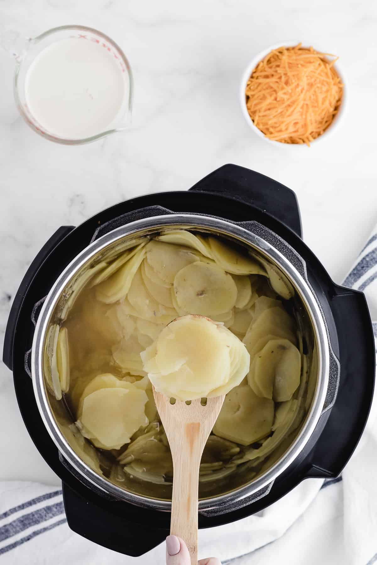 cooking sliced potatoes in a pressure cooker with some of the potatoes on a spoon
