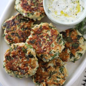 greek turkey burger patties on a white platter with a side of tzatziki sauce