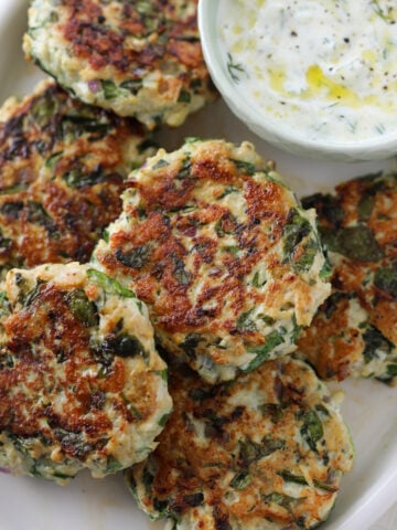 greek turkey burger patties on a white platter with a side of tzatziki sauce