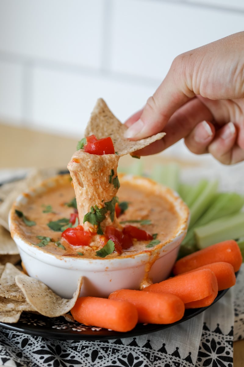 cottage cheese queso dip with a woman dipping a chip into the cheesy dip
