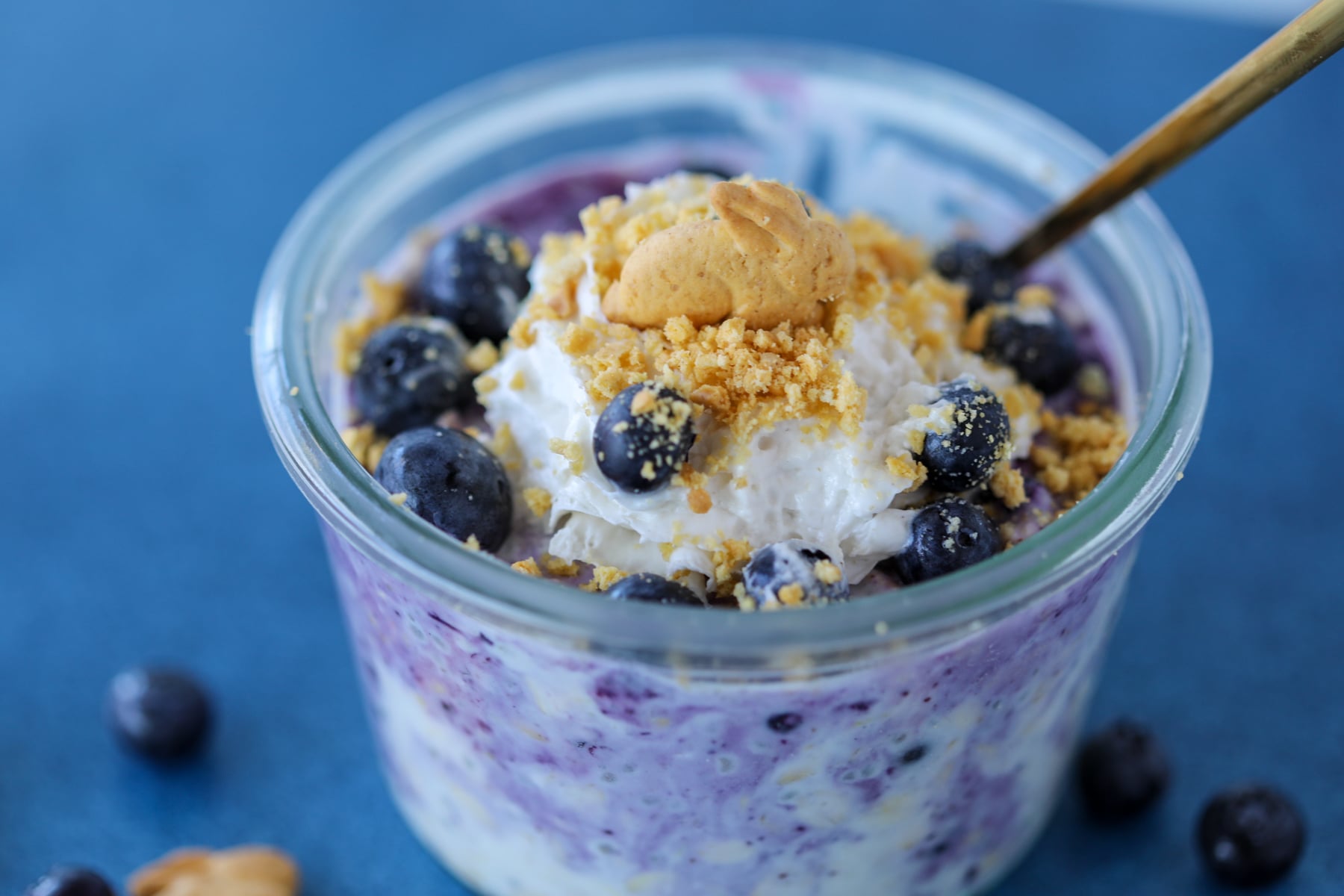 blueberry cheesecake overnight oats on a blue background with crushed graham cracker topping