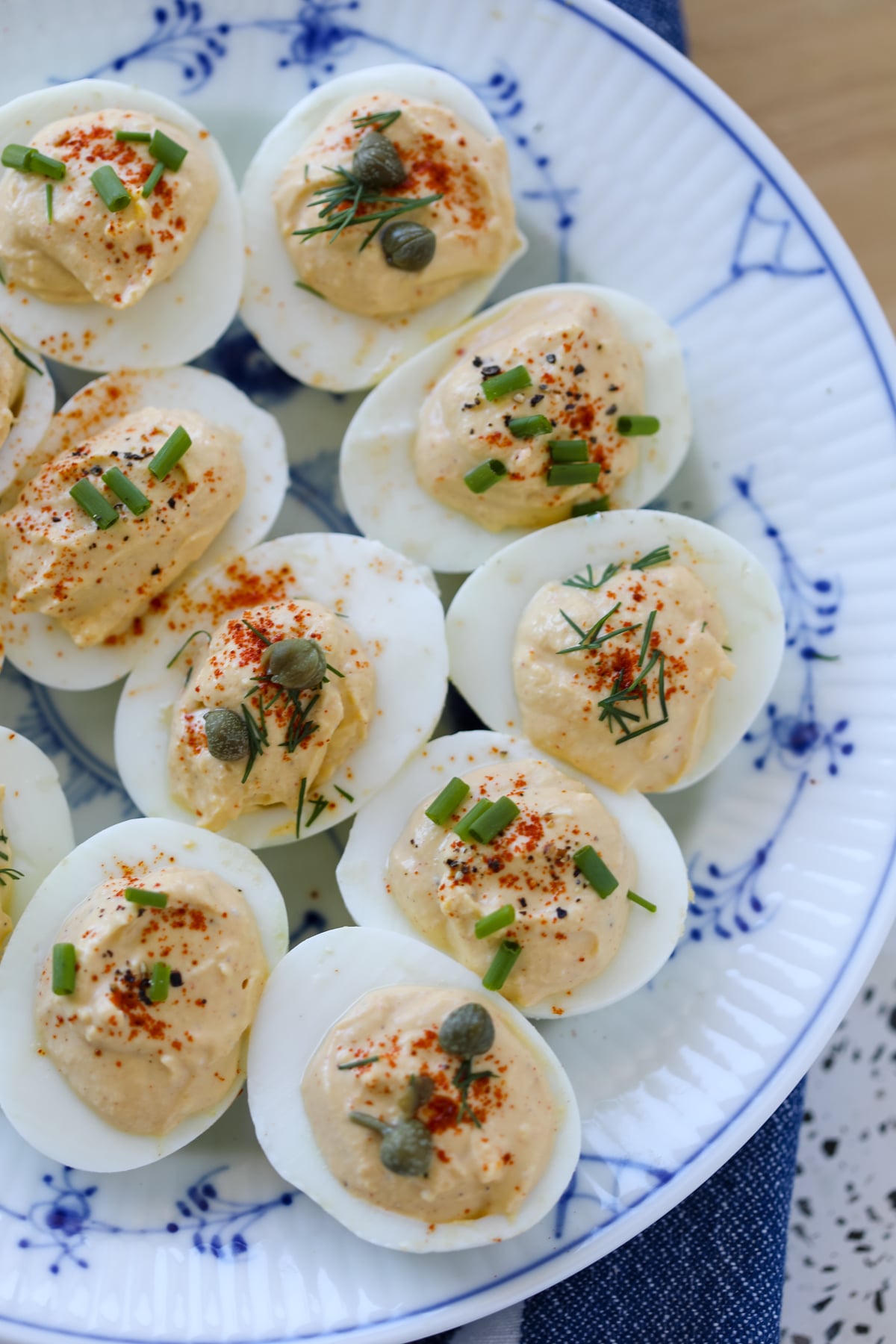 greek yogurt deviled eggs with dill capers and chives on a blue and white plate