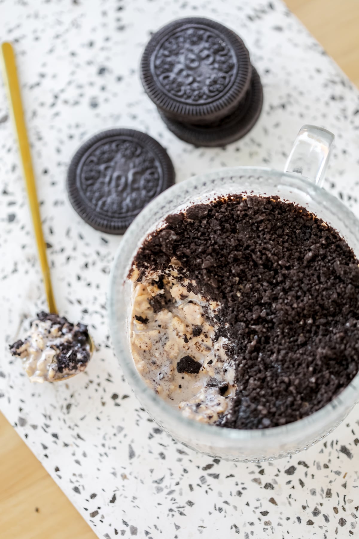 healthy oreo overnight oats with a spoon out of the oats on a white cutting board with stacks of cookies