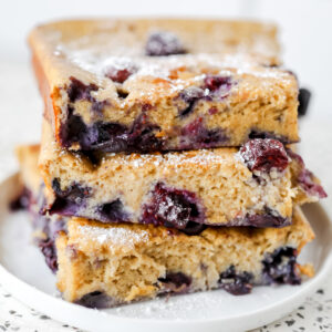 stacking up the blueberry cottage cheese breakfast bake slices on top of each other on a white plate frontal view