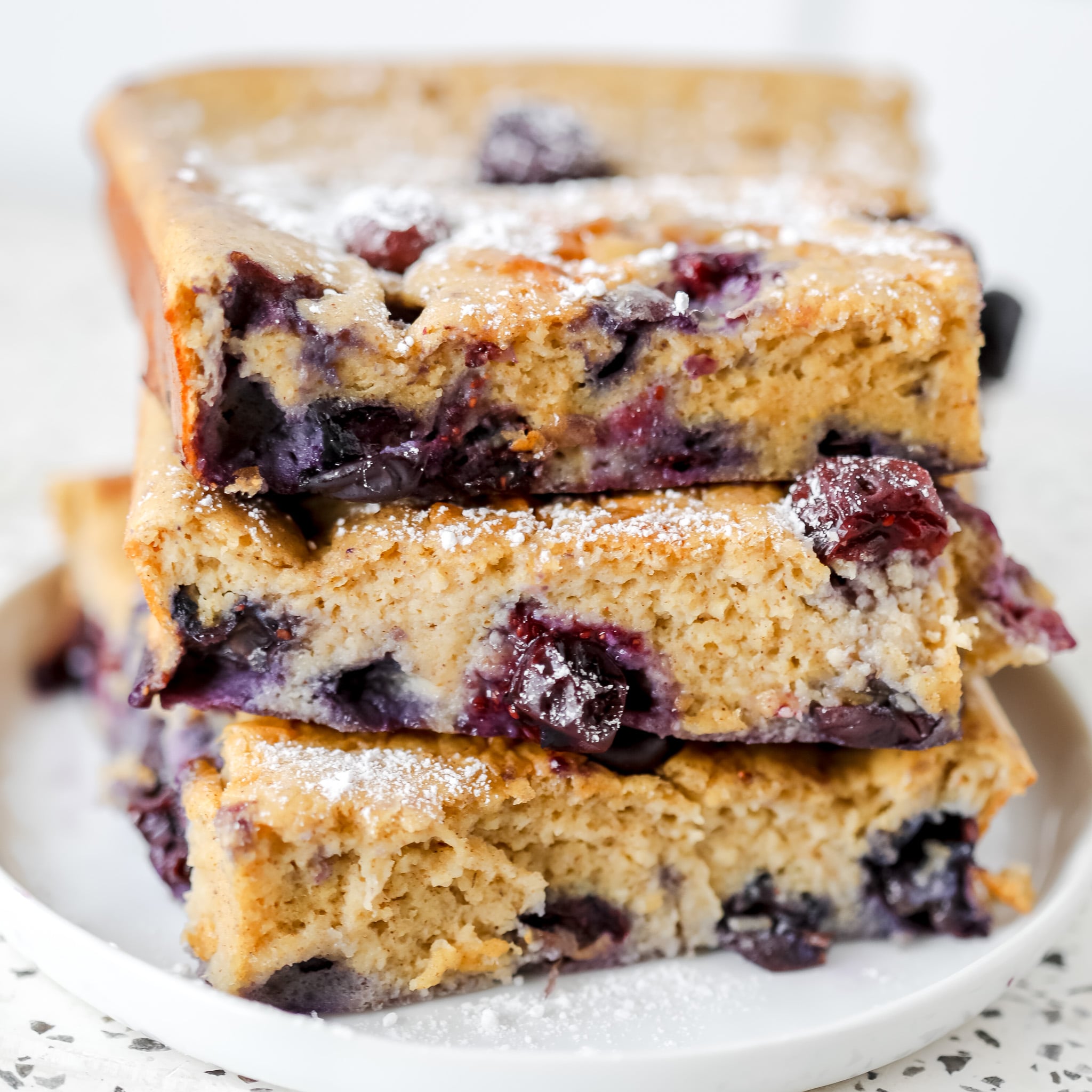 stacking up the blueberry cottage cheese breakfast bake slices on top of each other on a white plate frontal view