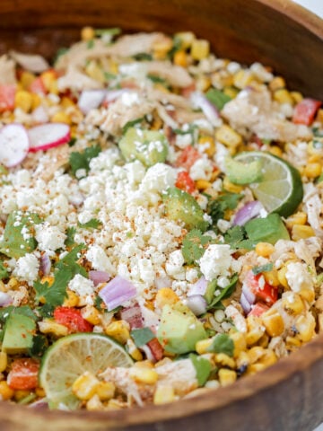 the mexican corn and chicken salad in a wooden bowl topped with cotija cheese lime cilantro and tajin