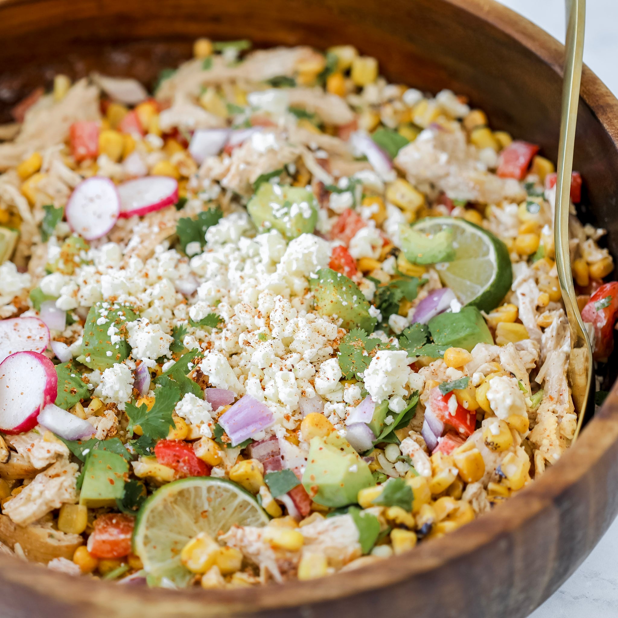 the mexican corn and chicken salad in a wooden bowl topped with cotija cheese lime cilantro and tajin