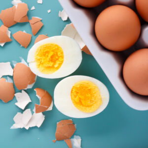 close up view of 555 instant pot eggs after pressure cooking on a blue background with one egg cracked open to see perfectly cooked yellow yolk