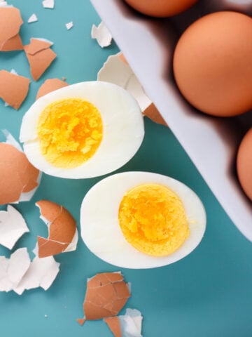 close up view of 555 instant pot eggs after pressure cooking on a blue background with one egg cracked open to see perfectly cooked yellow yolk