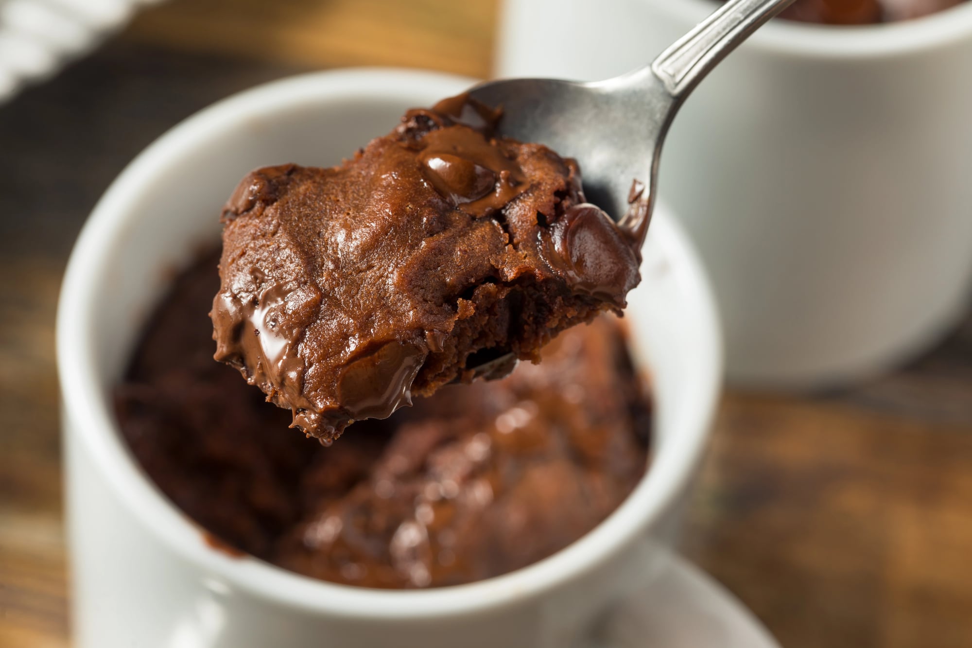 protein mug cake with chocolate protein powder in a white mug with a bite on a spoon
