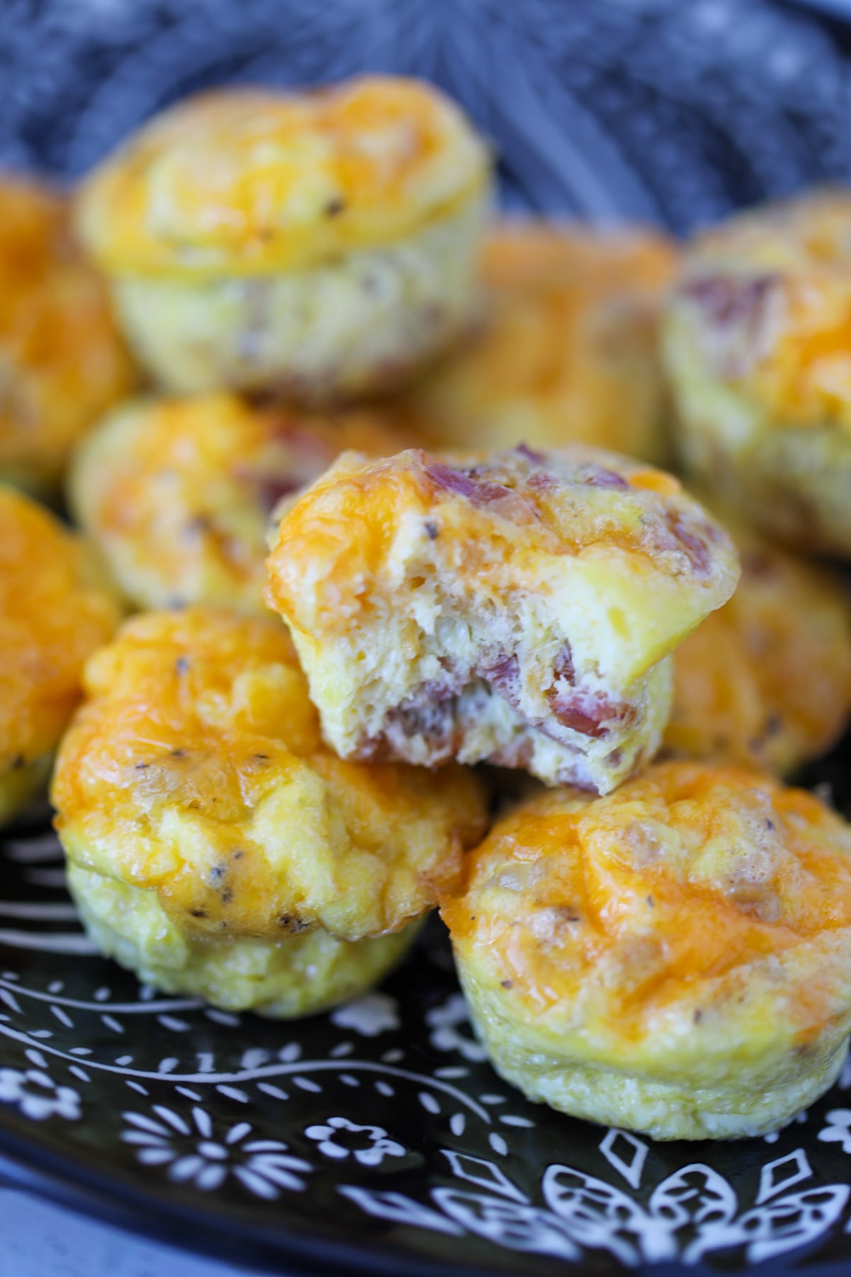 carnivore egg bites with sausage and bacon on a black plate with a bite out of one egg muffin