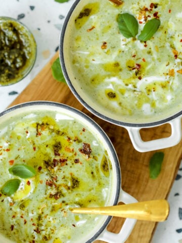Two bowls of creamy zucchini soup being served on a wooden board