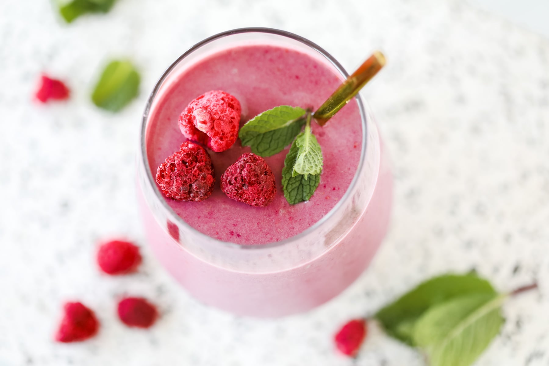 top down view of a healthy raspberry smoothie topped with mint and freeze dried rasberries on a marble background